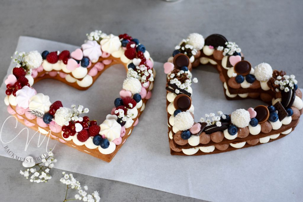 Zwei Herzkuchen in Herzform. Dekoriert mit Beeren, Süßigkeiten und Blumen.